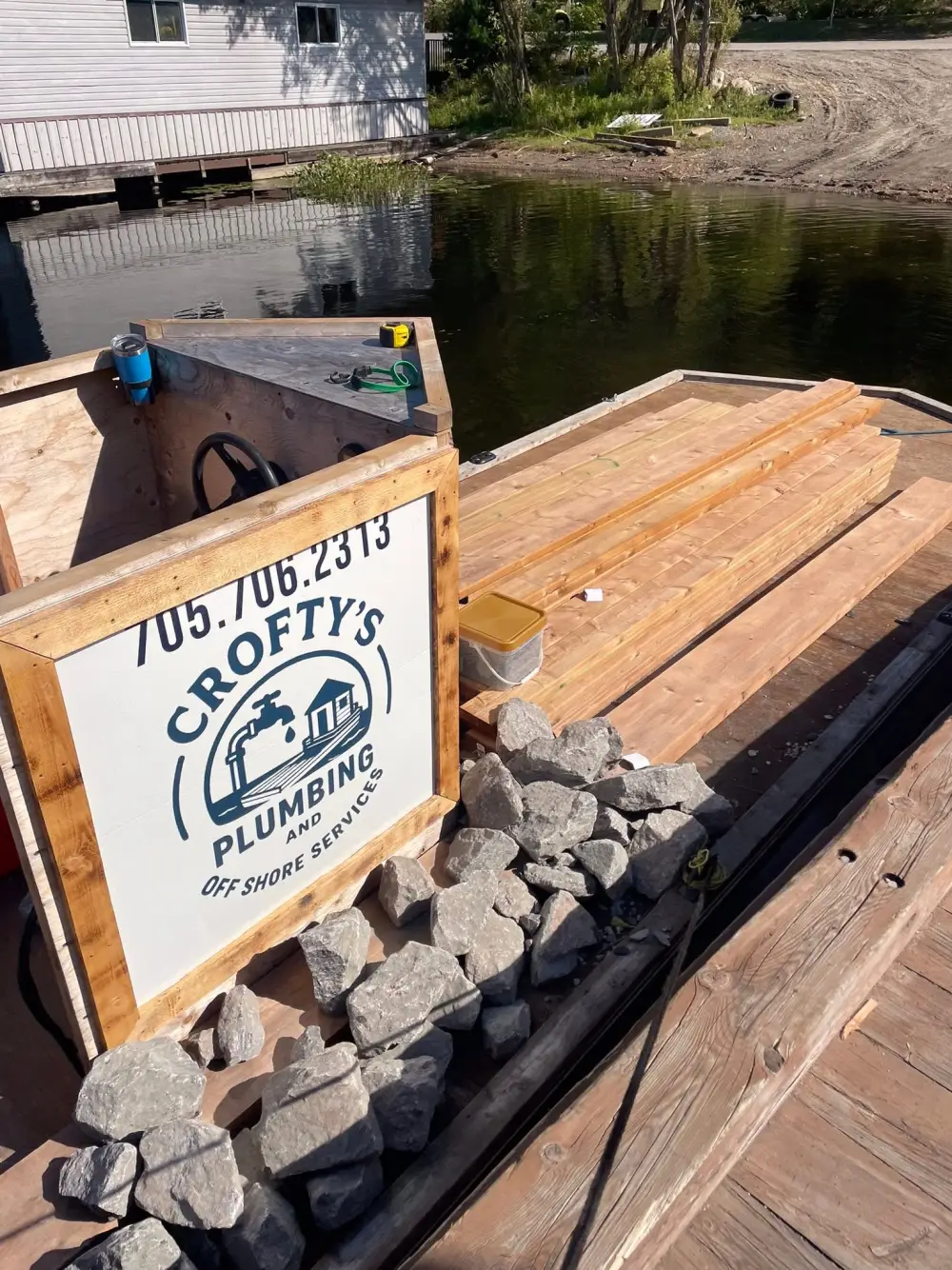 Crofty's Plumbing & Off-Shore Services work barge loaded with stone and materials beside a water-access cottage in Muskoka
